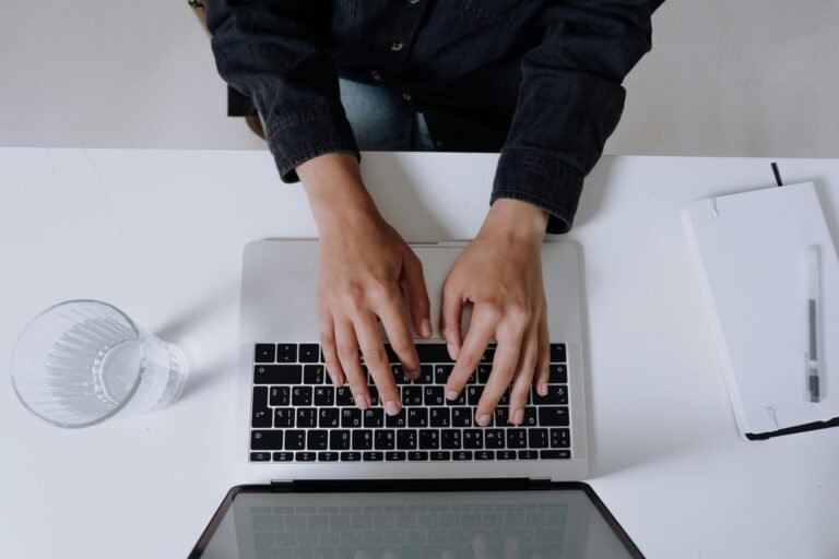Hands typing on a laptop keyboard viewed from above, capturing a modern work environment.