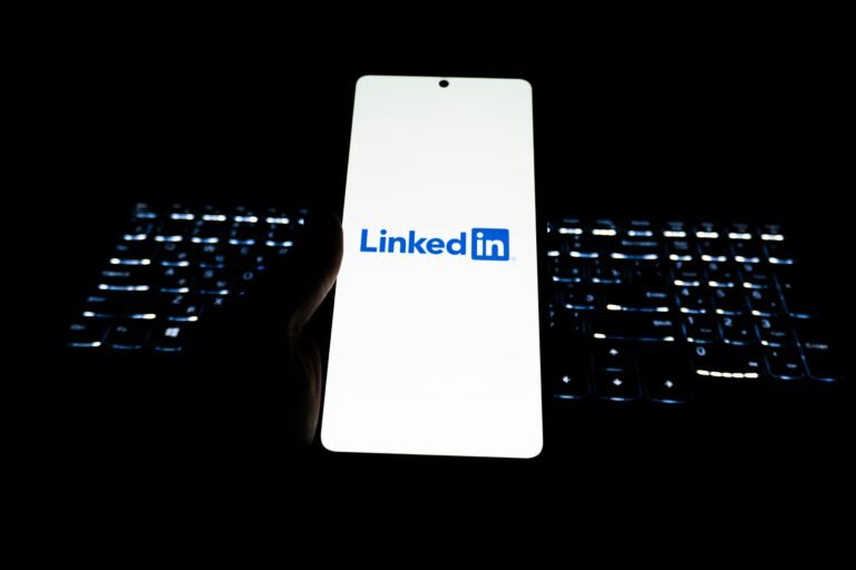 Close-up of LinkedIn logo on smartphone with backlit keyboard in dark room.